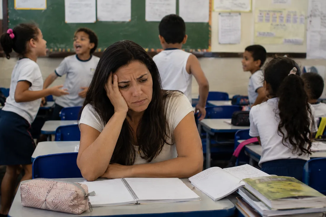 Professora exausta com a cabeça apoiada na mão enquanto os alunos se dispersam atrás dela